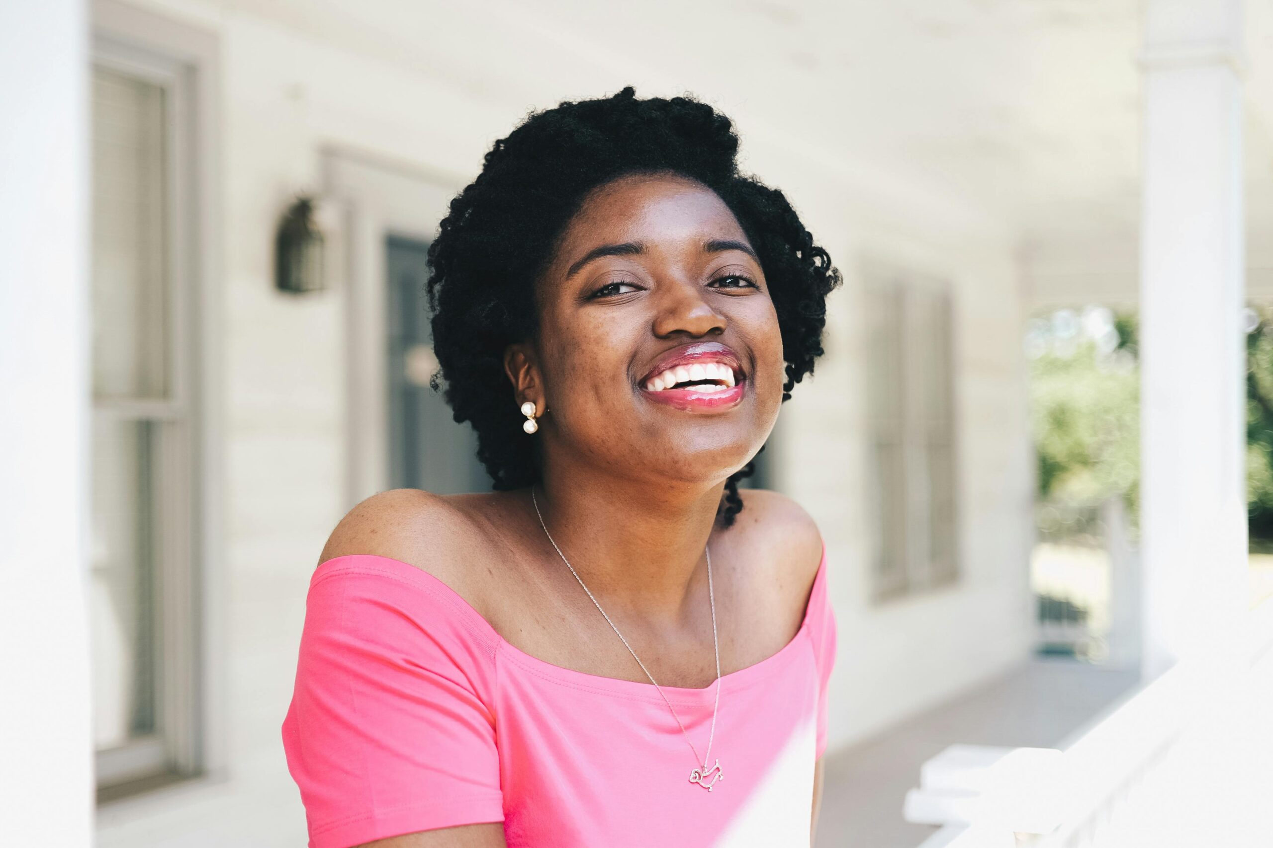 A beautiful woman in pink smiling warmly in an outdoor setting.
